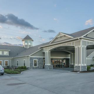 A modern building with a car parked in front and a cloudy sky overhead.