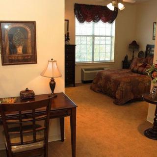 A cozy bedroom with a desk and lamp, featuring a large window and warm decor.