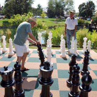 Two people engage in a game of giant chess at a park.