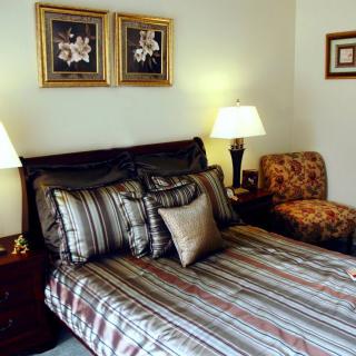 A well-decorated bedroom featuring a neatly made bed with striped bedding, accent pillows, bedside tables with lamps, and framed artwork on the walls.