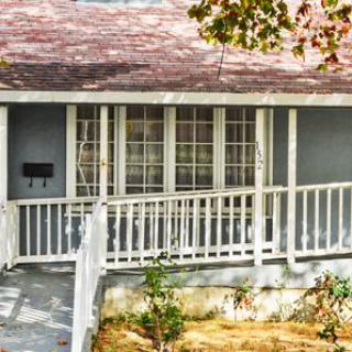 A cozy house with a porch and ramp surrounded by trees.