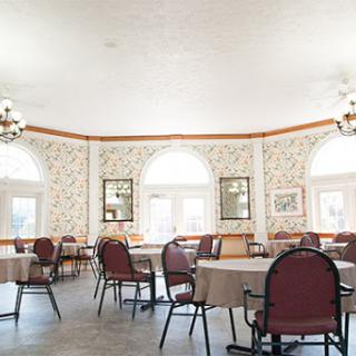 A spacious dining area featuring round tables and comfortable chairs, illuminated by natural light from large windows.