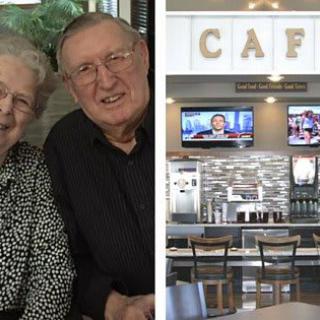 An elderly couple smiling beside a cafe interior with televisions.