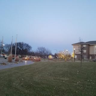 A peaceful park scene during the evening, featuring well-maintained grass and nearby buildings.