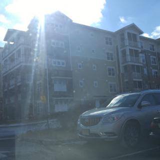 A modern apartment building with a parked car in the foreground, illuminated by bright sunlight.