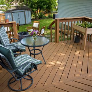 A cozy backyard deck featuring outdoor seating with striped cushions and a round glass table.