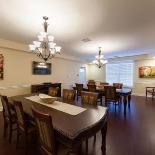 A spacious dining room with wooden floors, featuring two large tables and elegant chandeliers.