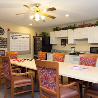 A well-organized meeting room featuring a long conference table with chairs and an adjacent kitchen area.