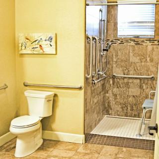 An accessible bathroom with a walk-in shower, grab bars, and tiled walls.