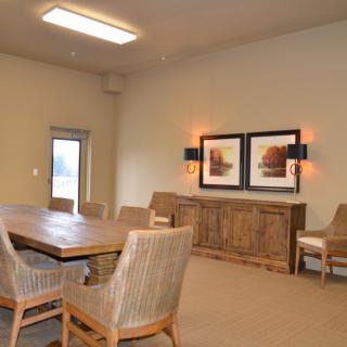 A dining room with a wooden table, several chairs, and framed artwork on the wall.