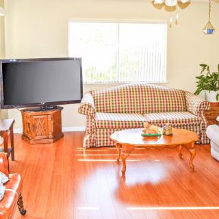 A cozy living room with a checkered sofa, wooden flooring, and a large television.