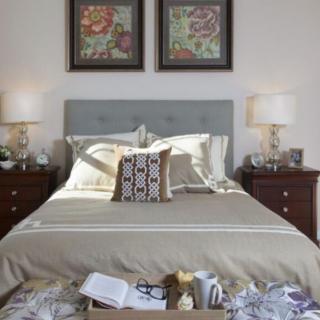 A cozy bedroom scene featuring a neatly made bed with decorative pillows, flanked by wooden nightstands and elegant lamps, with framed artwork on the wall.