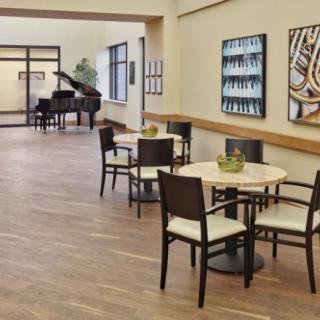 A modern lobby with tables and chairs, featuring artwork on the walls and a grand piano in the corner.