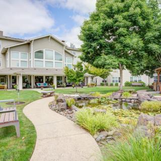 A serene garden with a winding pathway, benches, and a pond in front of a residential building.