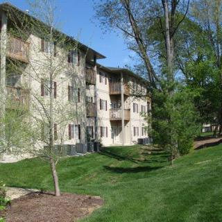 A residential apartment building surrounded by lush greenery and trees on a sunny day.