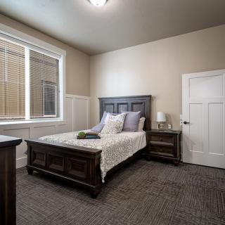 A cozy bedroom featuring a wooden bed and nightstand, with a large window allowing natural light.