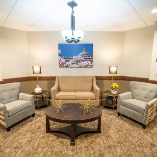 A cozy waiting room with armchairs and a sofa surrounding a coffee table under soft lighting.