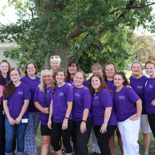 A group of people wearing purple shirts posing together outdoors.