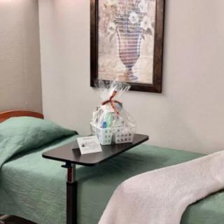 A hospital room with a bed, a gift basket on a tray table, and a painting on the wall.