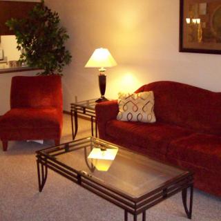 A cozy living room with a red sofa, matching chair, glass coffee table, and a lamp.