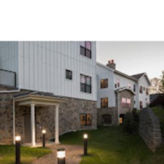A modern residential building showcasing a blend of stone and siding with outdoor lighting along the pathway.