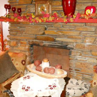 A cozy autumn-themed fireplace with rustic stonework, featuring candles and decorative leaves.