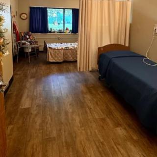 A hospital room with two beds separated by a curtain, featuring a window and basic furnishings.