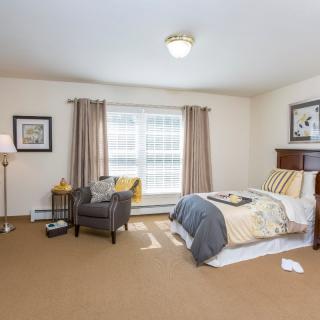A cozy and well-furnished bedroom with a bed, armchair, and natural lighting.