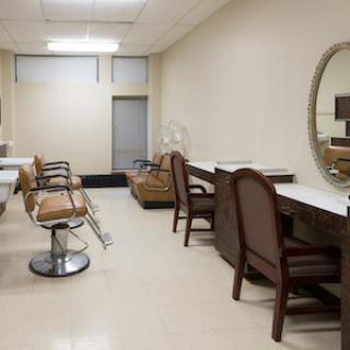 An empty beauty salon with chairs and mirrors arranged along the walls.