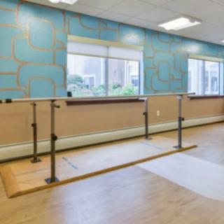 A spacious dance studio with a ballet barre and wooden floors, featuring large windows for natural light.