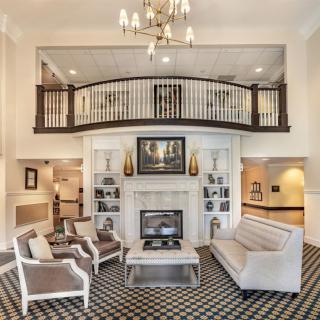 Elegant living room with a chandelier and balcony overlooking a seating area surrounding a fireplace.
