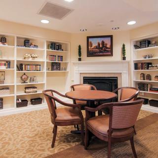 A cozy reading room with bookshelves, a table, chairs, and a fireplace.