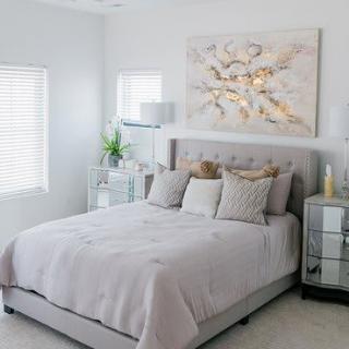A modern and minimalist bedroom featuring a neatly made bed with neutral colors, decorative pillows, and abstract artwork on the wall.