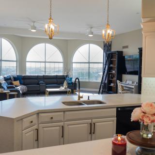 A modern open floor plan kitchen and living room with large arched windows and stylish pendant lights.