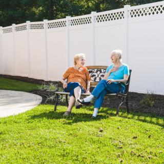 Two elderly women sitting on a bench, enjoying a conversation in a sunny garden.