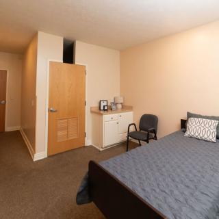 A cozy, minimalist bedroom with a bed, nightstand, and chair.