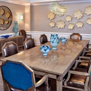 A stylish dining room featuring a large wooden table with blue-backed chairs, decorative vases, and wall art.