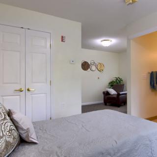 A cozy bedroom featuring a neatly made bed, decorative wall hangings, and a spacious closet with double doors.
