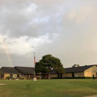 A suburban home with a large lawn, featuring a cloudy sky and a faint rainbow.