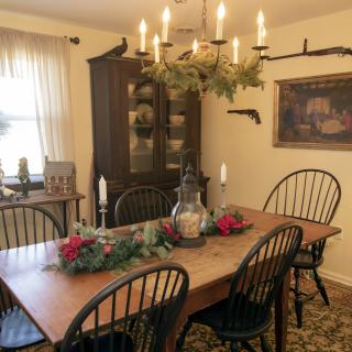 A cozy dining room with a wooden table, surrounded by chairs and decorated with greenery and candles under a rustic chandelier.