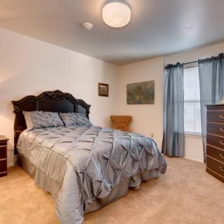 A cozy bedroom with a neatly made bed, a dresser, and drapes covering a window.