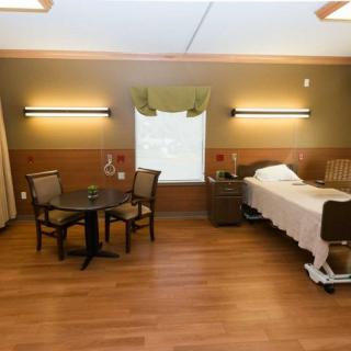 A well-lit hospital room with a bed, chairs, and a table near the window.