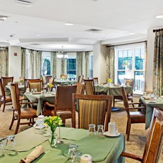 An elegant dining room with neatly arranged tables and chairs, adorned with natural light from large windows.