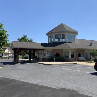 A view of a building with a covered entrance and parking lot under a clear blue sky.