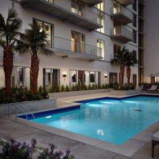 A well-lit apartment swimming pool surrounded by palm trees at night.