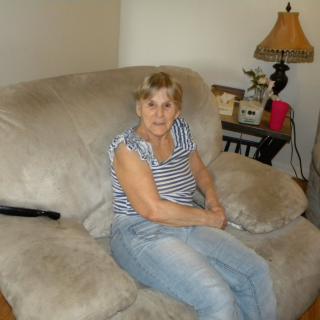 A woman sitting on a beige sofa in a living room with a lamp and table nearby.