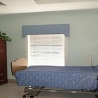 A simple hospital room with a single bed and a window with closed blinds.
