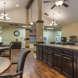 A spacious kitchen and dining area featuring dark wood cabinets, multiple chandeliers, and comfortable seating.