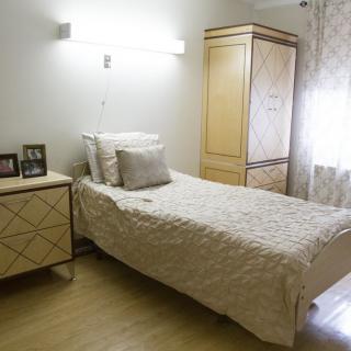 A minimalist bedroom featuring a single bed and light wooden furniture.