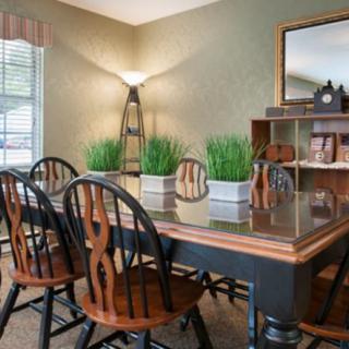 A cozy dining room with a wooden table, chairs, and decorative plants, featuring a lamp and mirror.